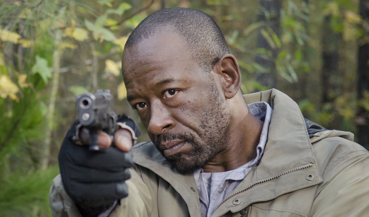Morgan, wearing a tan jacket, and aiming a gun straight ahead of him with his right hand.