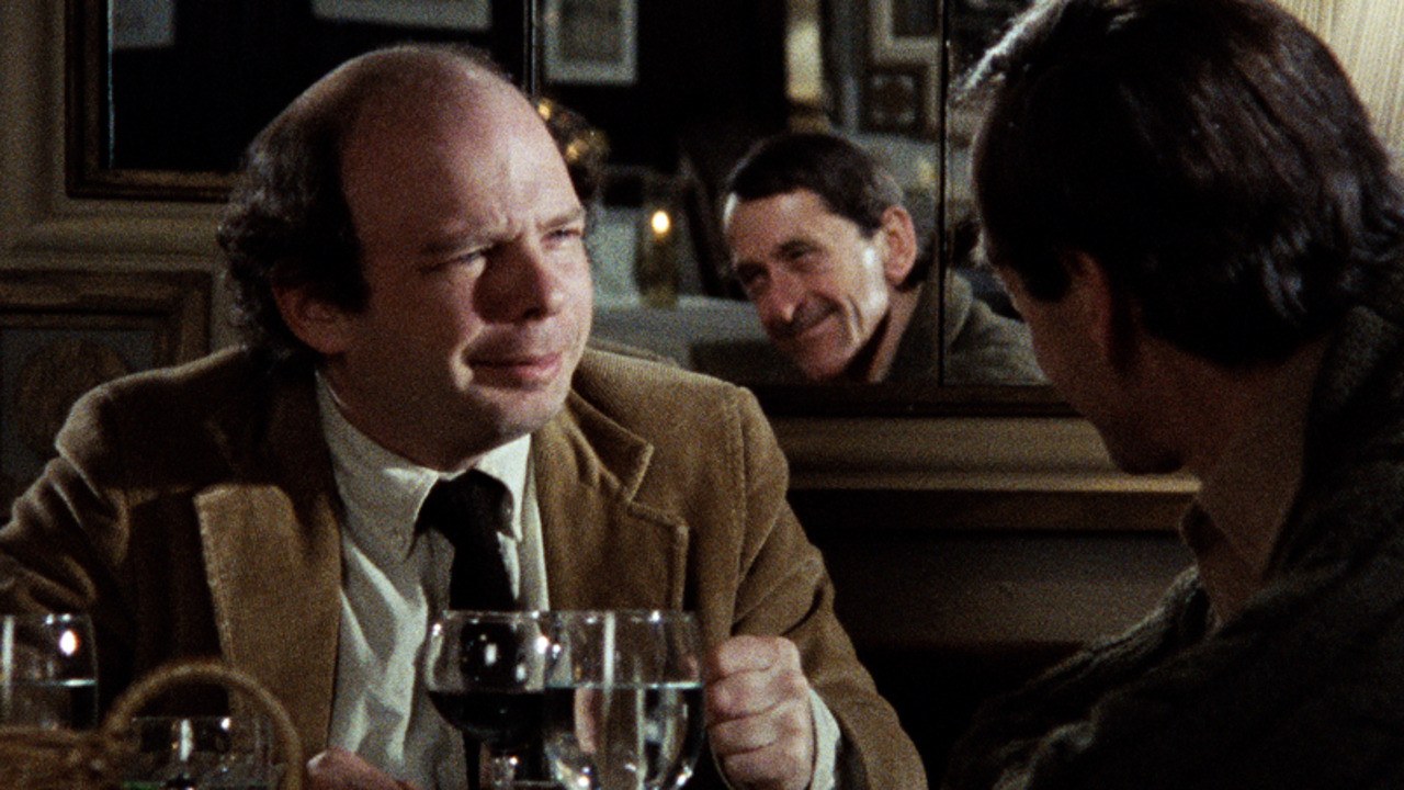 Wally Shawn, sitting across from a man in a restaurant, as the two have a deep conversation