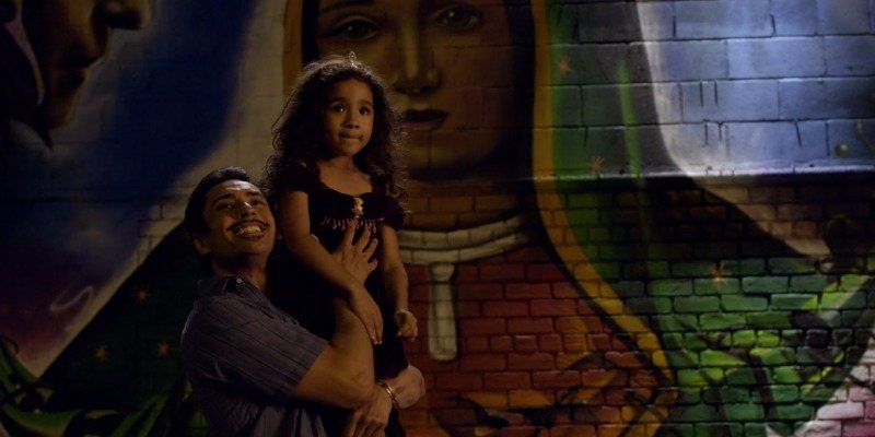 A father is holding up his little girl in front of a mural.