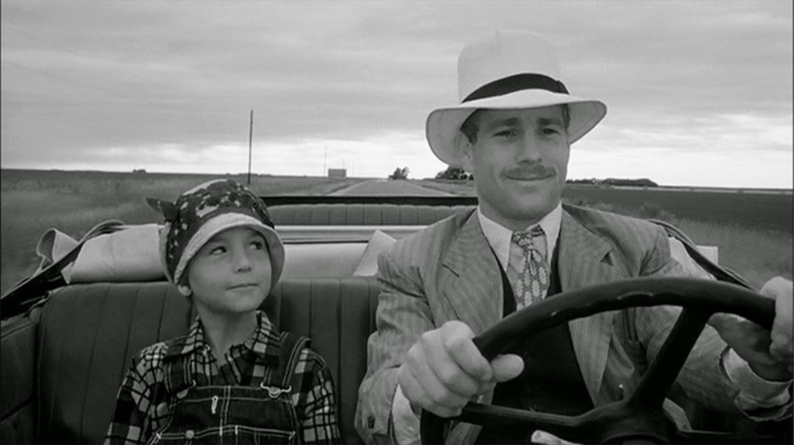A man and a small boy driving together, as they smile pensively