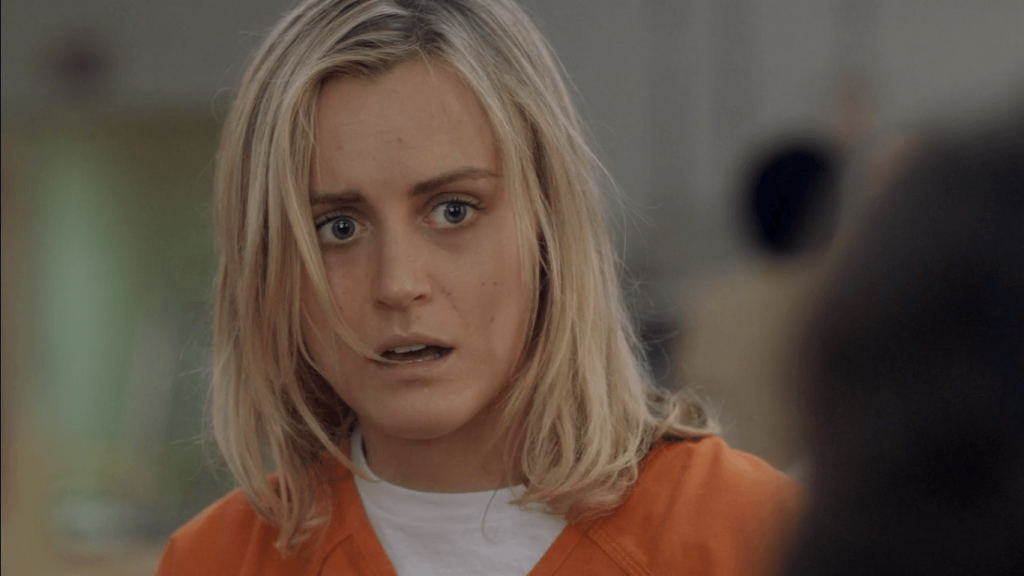 Piper, wearing an orange prison jumpsuit, and looking shocked off into the distance
