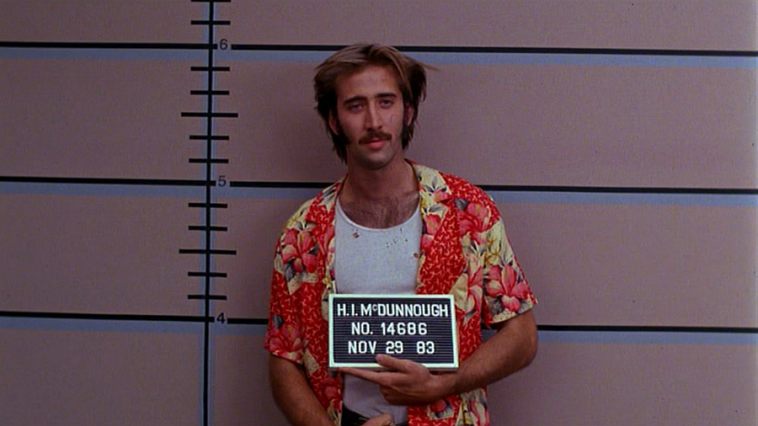 A young Nicolas Cage in Raising Arizona, in a mug shot wearing an orange floral button up shirt, opened over a white tank top