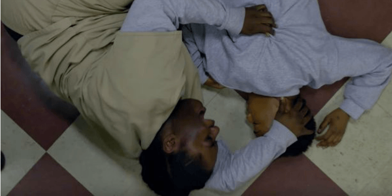 Taystee is crying on the floor next to Poussey.
