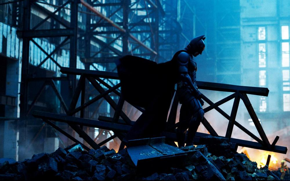 Batman, standing among rubble in the wake of an explosion