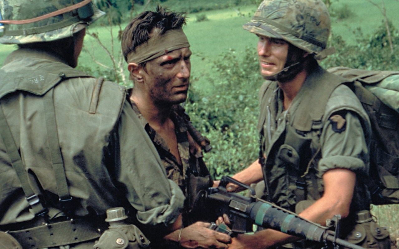 Three soldiers pose for a picture in the jungle of Vietnam, looking grimly into the camera