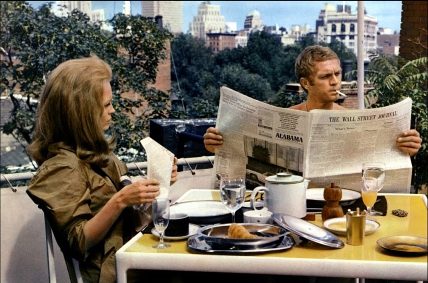 Steve McQueen sitting at a breakfast table reading a newspaper, while Faye Dunaway looks on