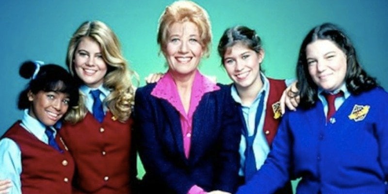The cast of The Facts of Life are posing together in front of a green background.