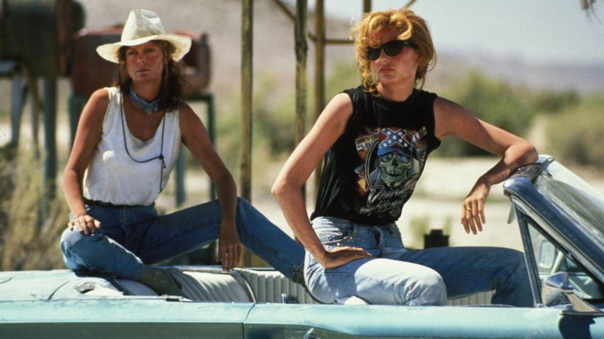 Geena Davis and Susan Sarandon, sitting on top of the seats in a blue convertible