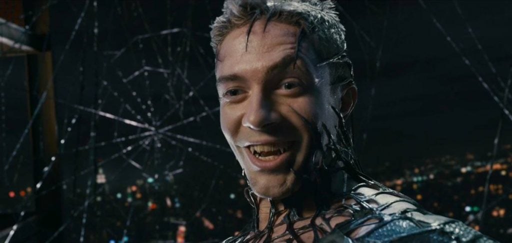 Topher Grace as Venom, with the Symbiote suit creeping up around his face while he smiles menacingly