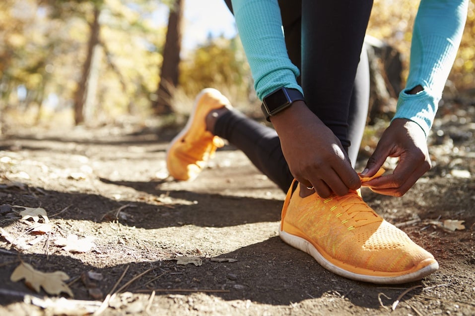 Black female runner in forest tying shoe
