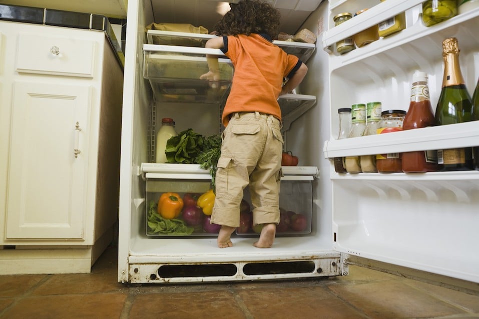 Boy standing in refrigerator looking for snack