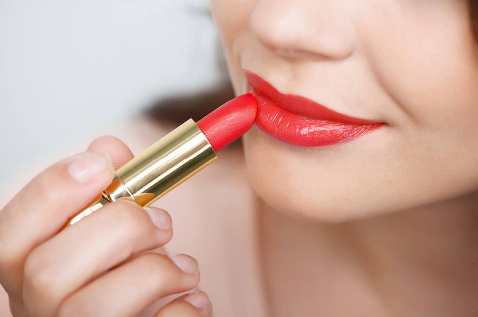 Young girl rouging her lips with red lipstick