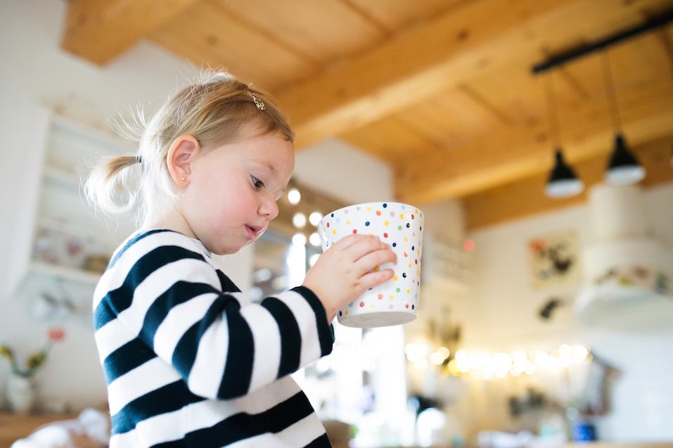 Cute little girl in striped dress sitting on kitchen table holding dotted tea cup