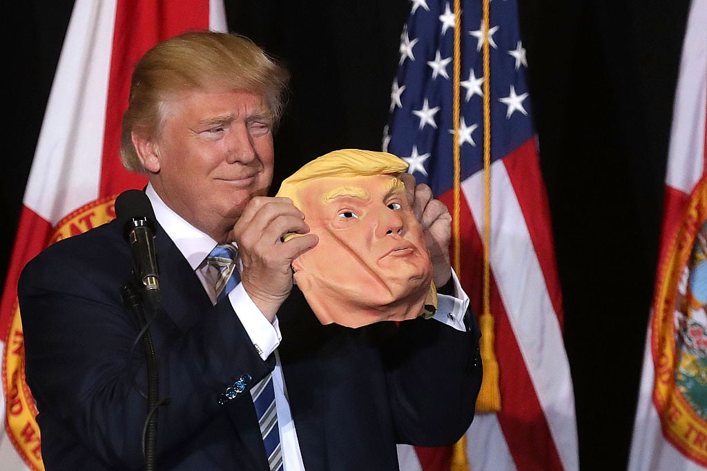 Donald Trump holds up a rubber mask of his face during a campaign rally