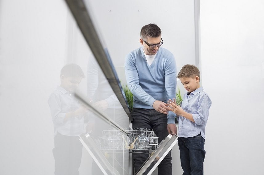 Father and son placing glass in dishwasher