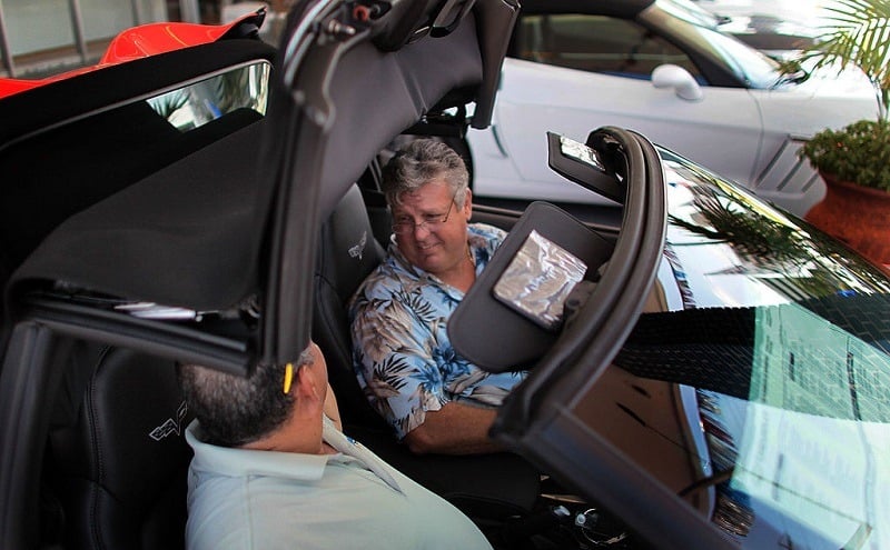 A car salesman talks to a customer while lowering the top of a convertible.