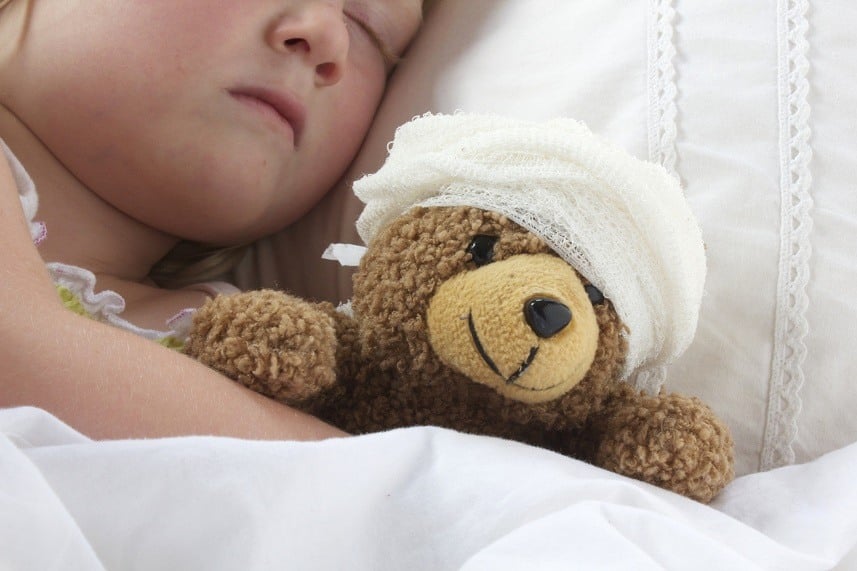 child in bed holding teddy bear