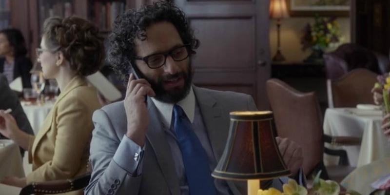 Jason Mantzoukas is in a suit and talking on a phone.