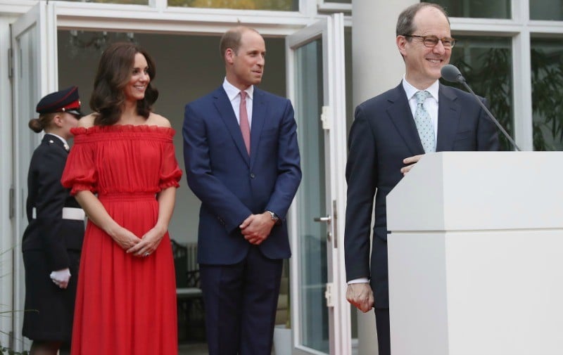 Kate Middleton is in a red strapless dress and is standing next to Prince William as an ambassador giving a speech. Kate Middleton is in a red strapless dress and is standing next to Prince William as an ambassador giving a speech.
