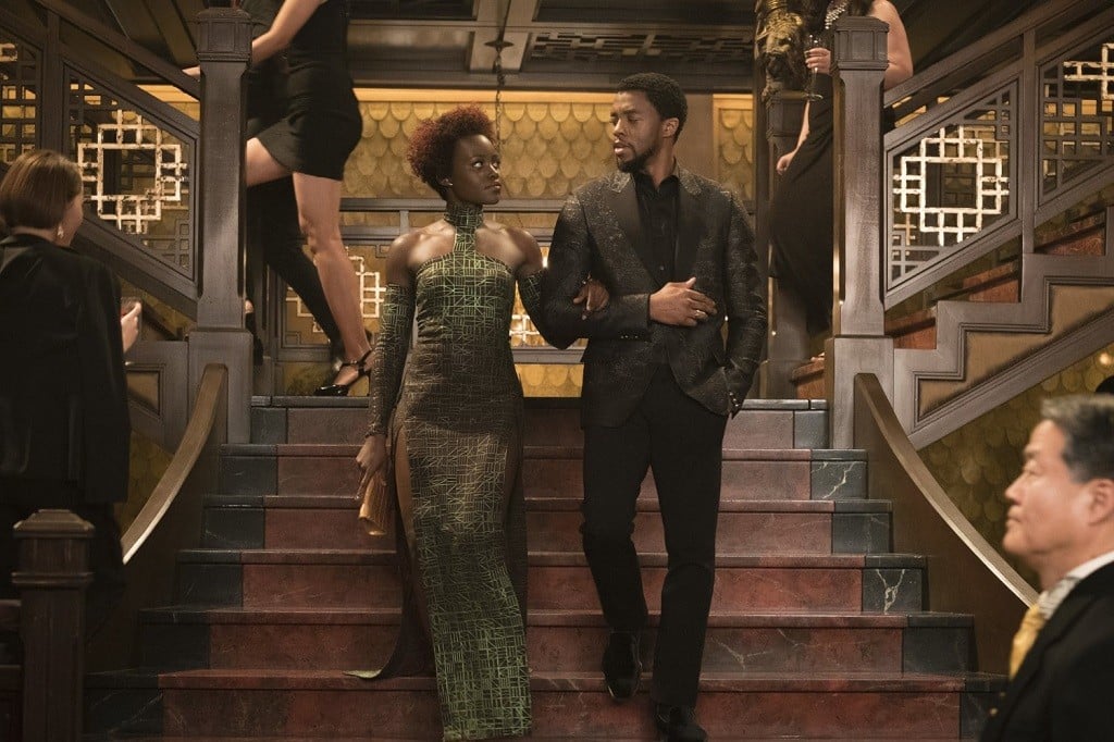 Lupita Nyong'o and Chadwick Boseman in formal wear descending a staircase.
