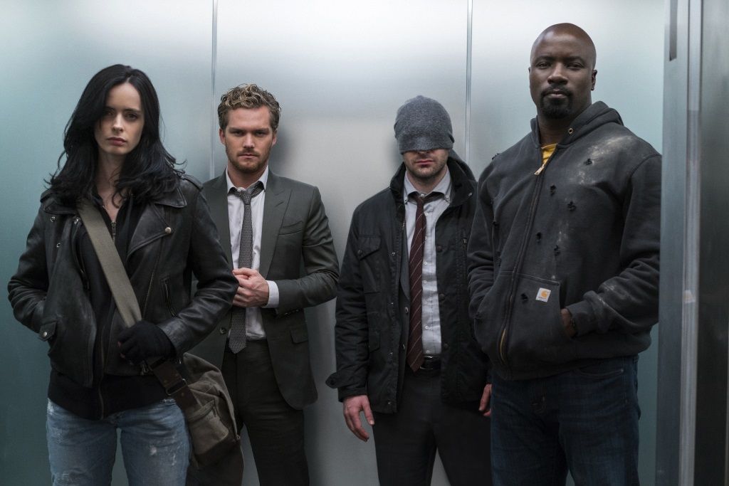 Krysten Ritter, Finn Jones, Charlie Cox, and Mike Colter standing in an elevator. Krysten Ritter, Finn Jones, Charlie Cox, and Mike Colter standing in an elevator.