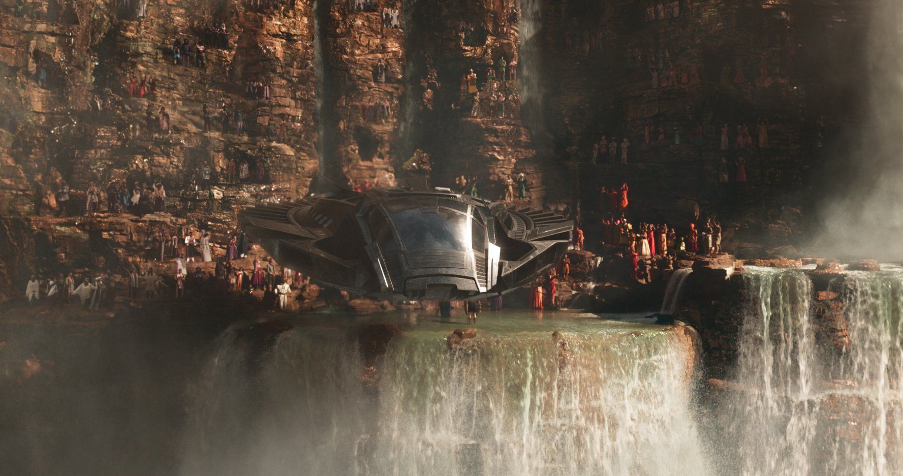 Many people gathered alongside a waterfall as a spacecraft hovers