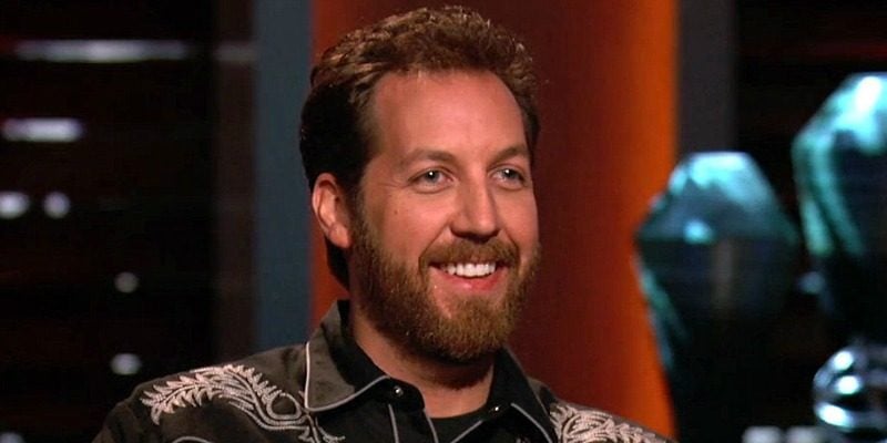 Chris Sacca is smiling as he sits on the set of Shark Tank.