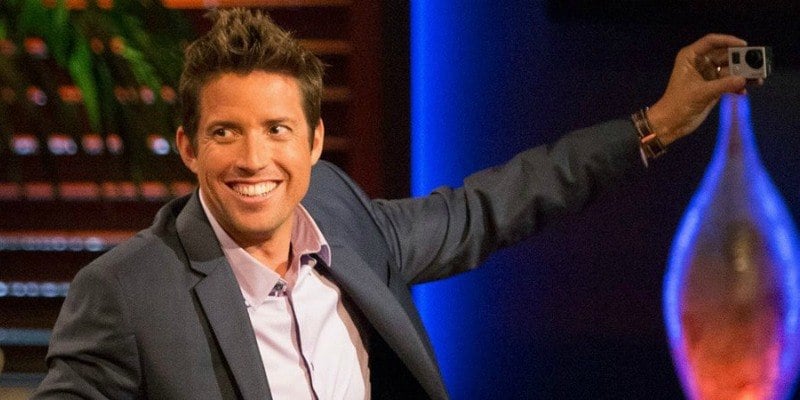 Nick Woodman is smiling and taking a picture of himself with a small camera on Shark Tank.
