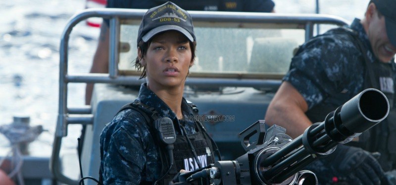 Rihanna is in a Navy uniform behind a gun.