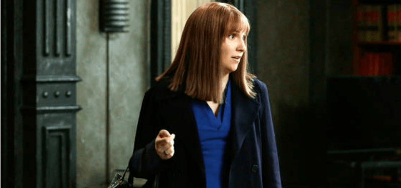 Lena Dunham is in a longer brown wig in an office.