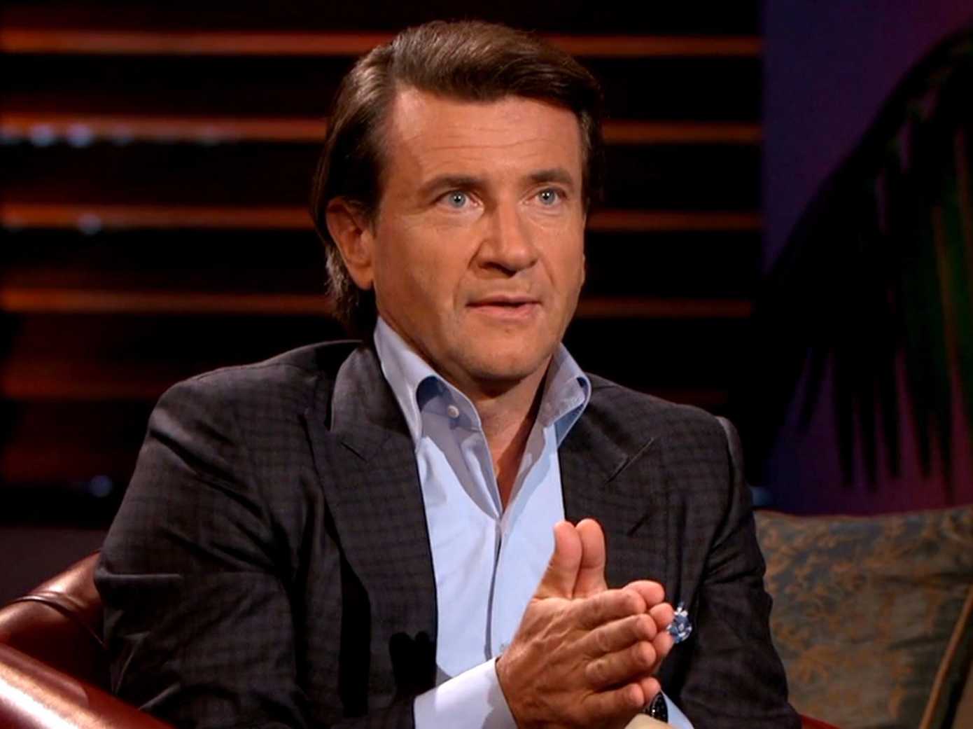 Robert Herjavec holds his hands together and learns forward in his chair on Shark Tank
