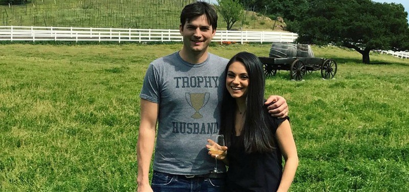Ashton Kutcher has his arm around Mila Kunis as they stand in a field.