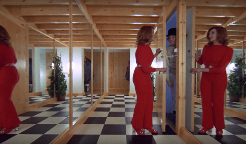 A woman in red opens a door in a mirrored hallway in A Clockwork Orange