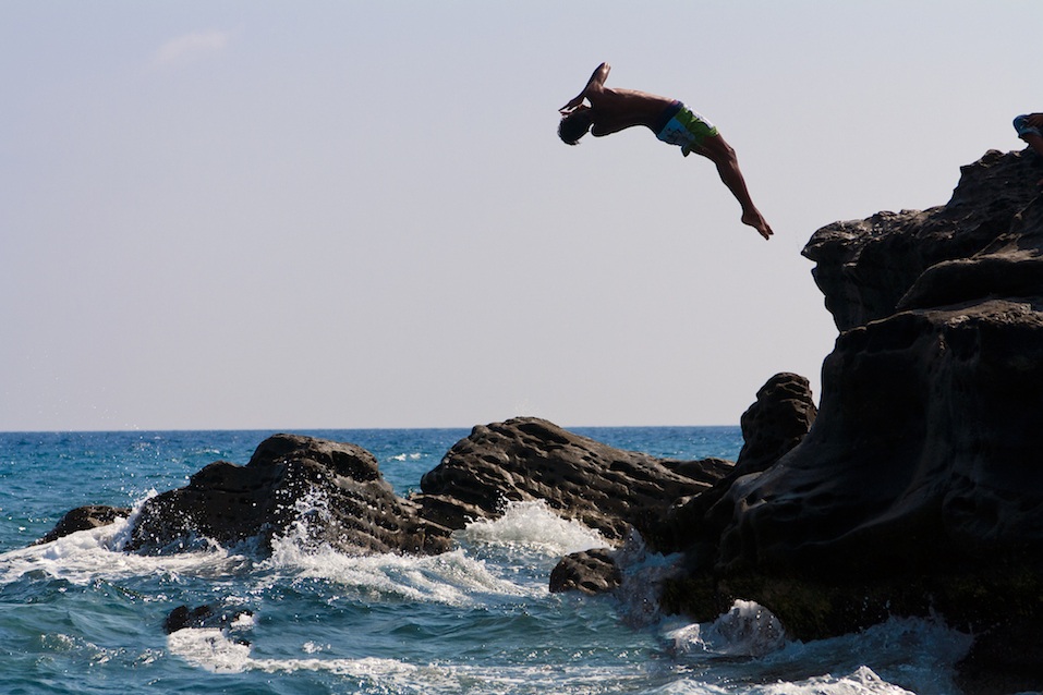 A man that is jumping from the rocks into the sea