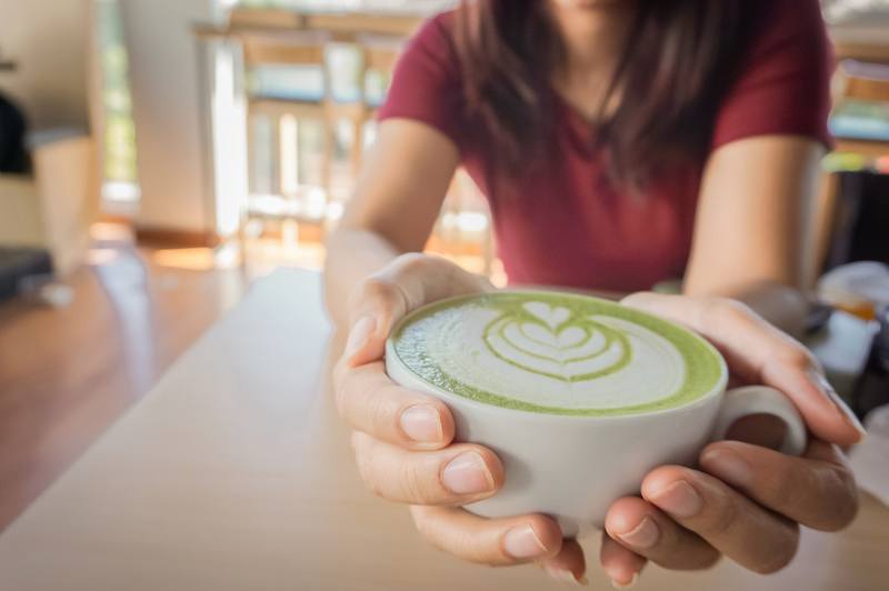Woman holding a cup of hot matcha green tea in her hands Woman holding a cup of hot matcha green tea in her hands