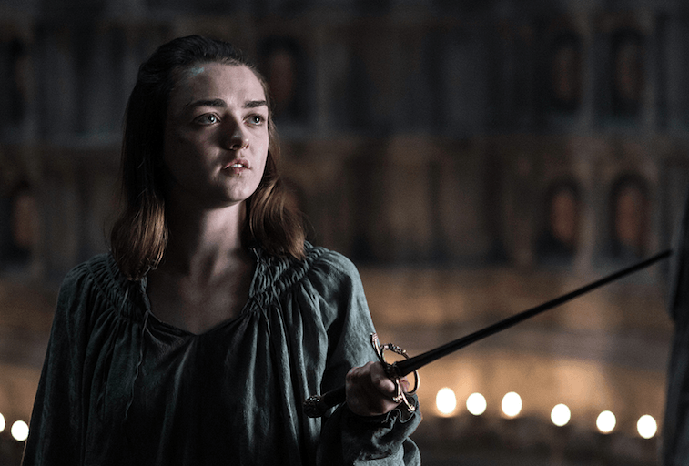 Arya stands holding her sword.