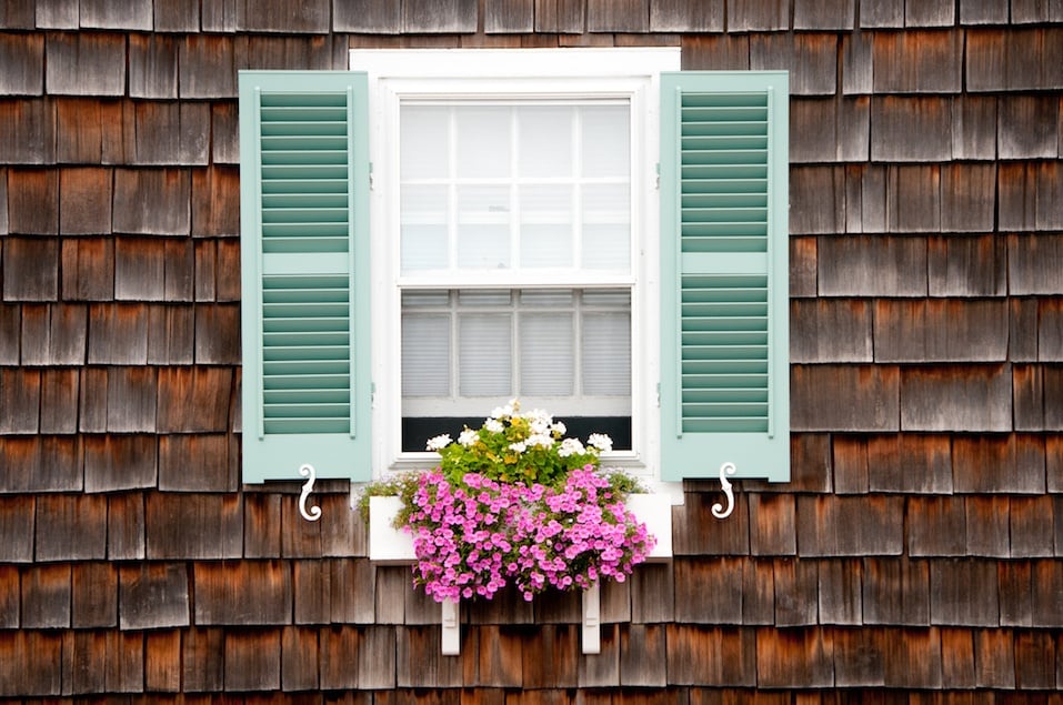 Window with turquoise shutters and white wooden window box and trailing pink and white flowers in summer