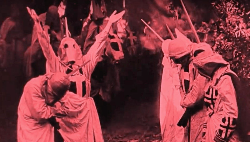 Men in white robes and masks throw up their hands in The Birth of a Nation Men in white robes and masks throw up their hands in The Birth of a Nation
