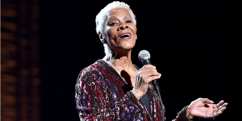 Dionne Warwick sings into a microphone on stage.