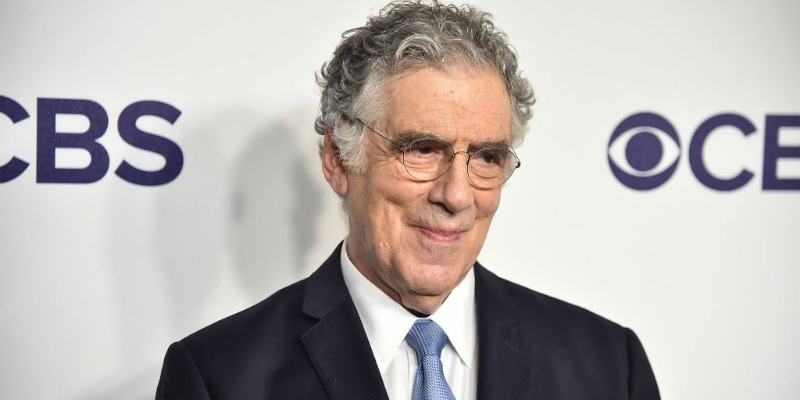 Elliott Gould is smiling in a suit on the red carpet.