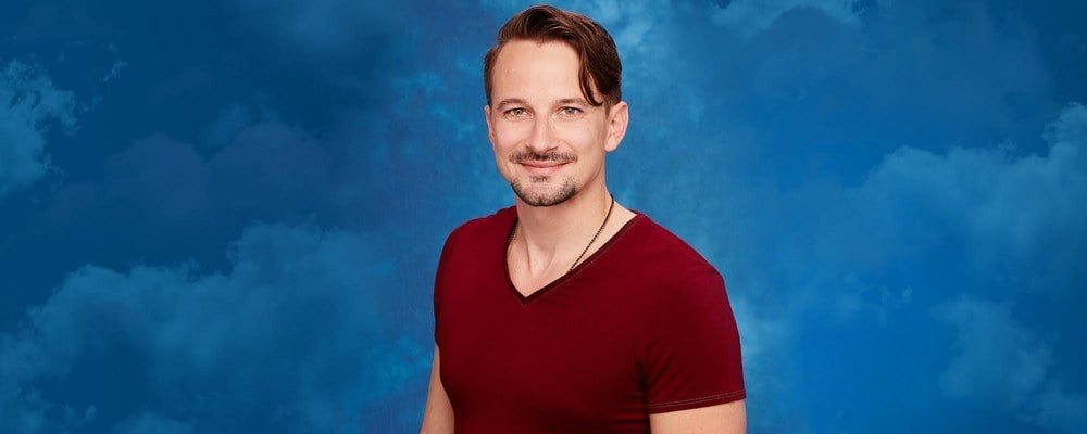 Evan Bass stands in front of a blue background wearing a red shirt. Evan Bass stands in front of a blue background wearing a red shirt.