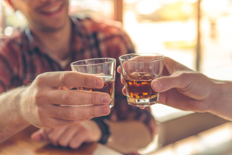 two men clanging glasses of alcoholic beverage together