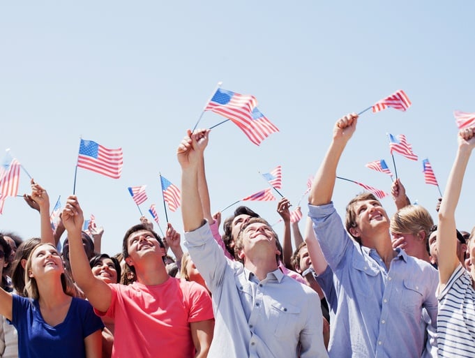Smiling people waving American flags and looking up in crowd