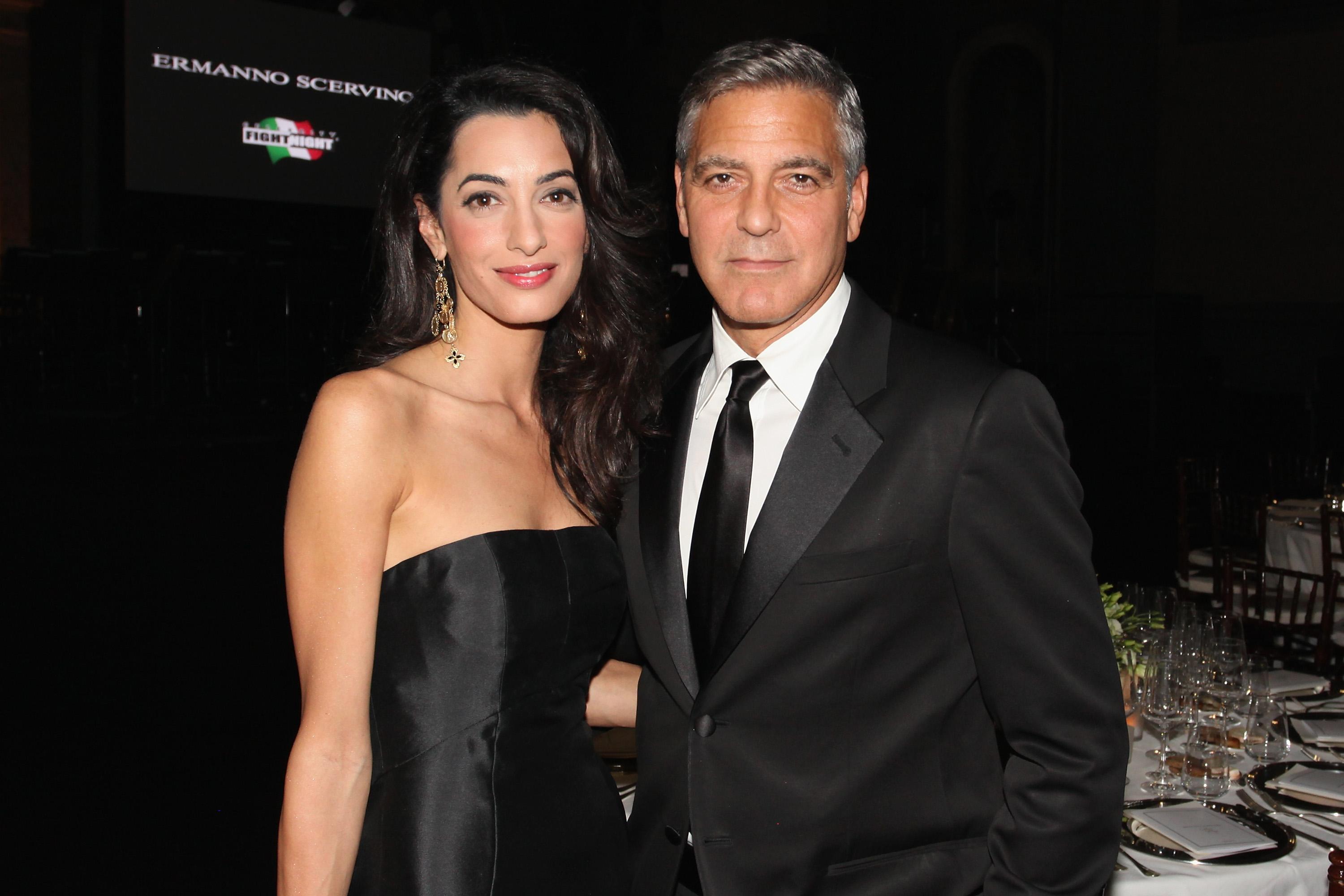 George and Amal Clooney wearing black and posing with their arms wrapped around each other. 