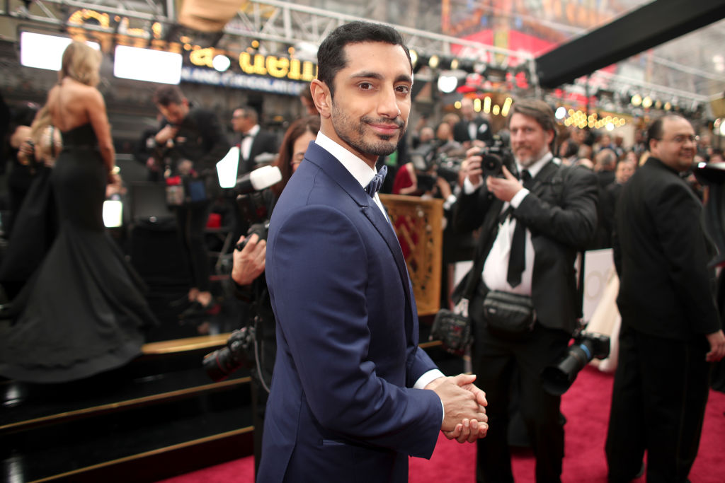 Riz Ahmed on the red carpet at the Oscars surrounded by cameras.