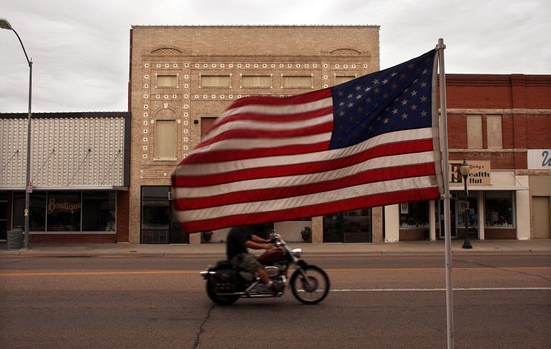 SIDNEY, NE - JUNE 26: A man rides his motorcycle down a flag laden street June 26, 2007 in Sidney, Nebraska. When rural America was chronicled 50 years ago by Jack Kerouac in his autobiographical novel "On the Road", it was an America full of promise and economic potential, where the majestic openness of the land was entwined with the cult of the automobile. Today, partly due to the loss of the independent family farm, rural America is a state of economic and demographic decline. Despite these changes since Kerouac and his friends sped across the vast American night, much of the visual landscape of the rural United States has remained the same. 