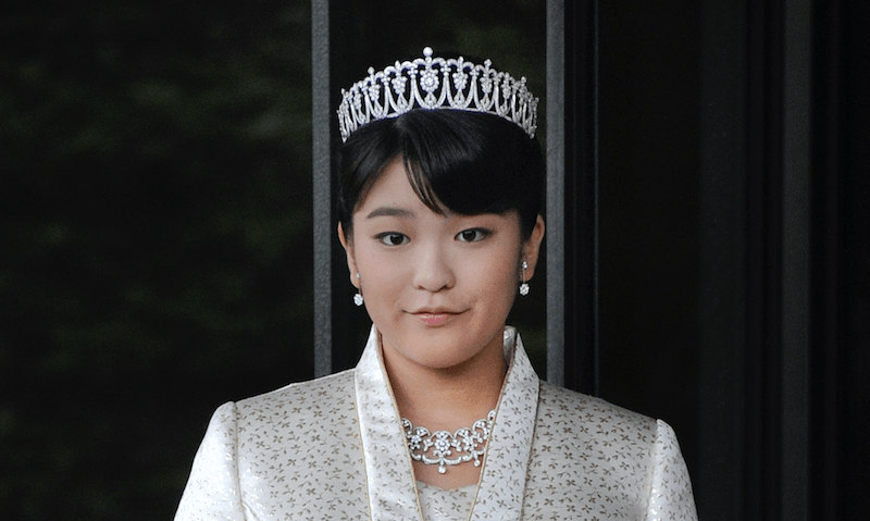 Princess Mako stands in a white suit and a crown.
