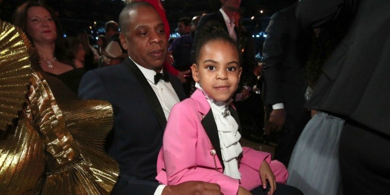 Blue Ivy is sitting on Jay Z's lap in a pink suit. Blue Ivy is sitting on Jay Z's lap in a pink suit.