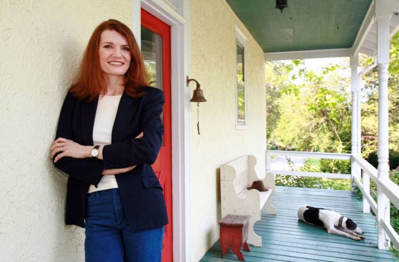 Jeannette Walls leaning up against a house standing on a porch with a dog in the background