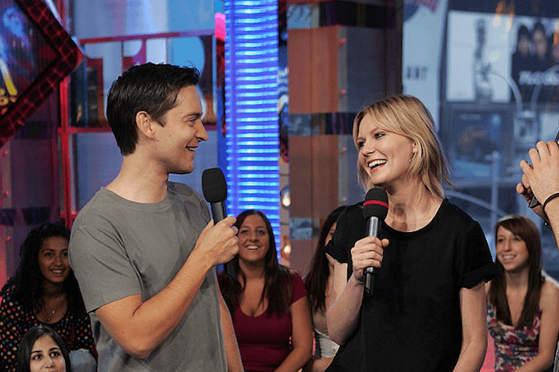 Toby Maguire and Kirsten Dunst hold up microphones while being interviewed on camera.